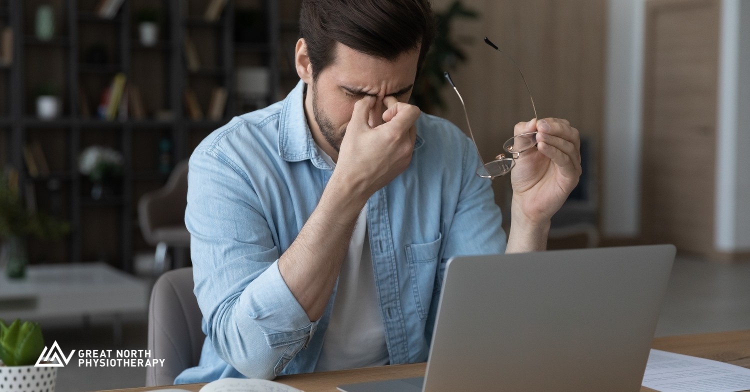 A man is sitting at a computer with his glasses off and his hands on his eyes because he is experiencing a bout of vertigo