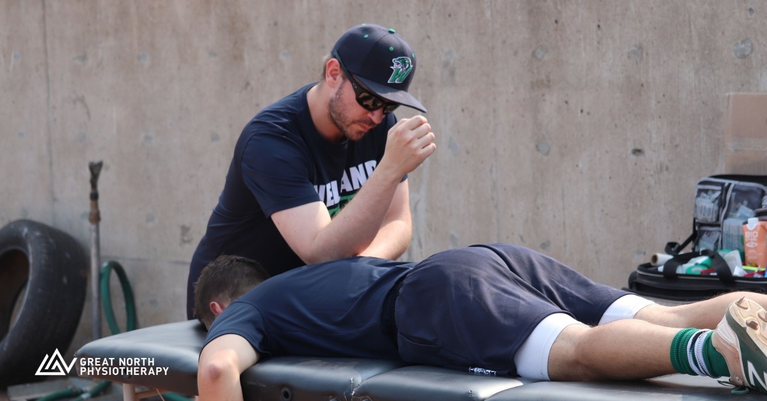 Trevor Kwolek Sports Physiotherapist is doing manual therapy on a Welland Jackfish baseball player beside the dugout